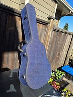 Closed blue denim guitar case standing upright showing exterior fabric, latches, handle