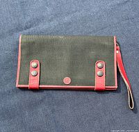 Front view of black canvas clutch with red leather trim, front snap tabs, wrist strap attached