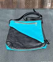 Front view of turquoise and black crossbody bag showing exterior zip pocket and strap