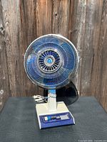 Front view showing full fan with blue blades, ivory stand, control panel