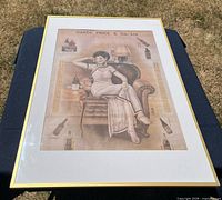 Full view of framed advertisement print on table, gold frame, white mat, image content visible