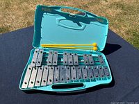 Open teal case showing full 25-note glockenspiel and both yellow mallets positioned above bars