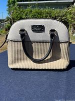 Front view showing woven straw body, pebbled leather top, black handles, gold-tone logo plaque
