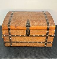 Front view of wooden trunk showing curved lid, metal straps, studs, and lock latch