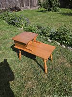 Full view of honey oak two-tier telephone table standing on grass