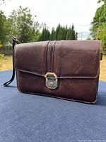Front view of brown leather clutch with wrist strap and clasp visible