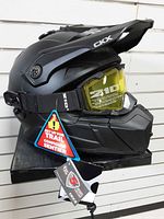 Left side profile of black CKX Titan helmet showing yellow goggles, chin guard, tags