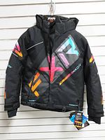 Front view of black FXR youth jacket with multi-color graphics, tags attached