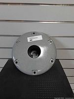 Top view of round silver/gray base with central hole, four mounting recesses, barcode label visible