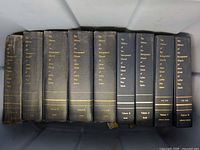 Eight gray cloth hardcover volumes with gilt titled spines laid in bin