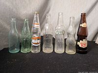 Front view of all seven glass bottles showing brands, colors and labels