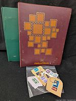 Front view of maroon Philatelia binder, green binder behind, and plastic bag with loose stamps