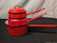Nested red enamel saucepans with lid showing size relation and handles