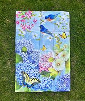 Flag with bluebirds amid hydrangeas, butterflies, hollyhocks