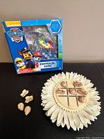 Both games together: boxed Paw Patrol Popper Jr. game and sunflower tic-tac-toe board with pieces on top