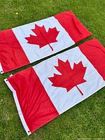 Two Canadian flags laid flat on grass showing full design