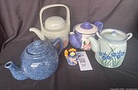 Group shot of four teapots and small figurine