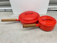 Large and small red enamel saucepans with lids, side view showing wood handles