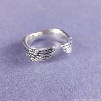 Angled view of silver wing wrap ring showing feather detail and open band