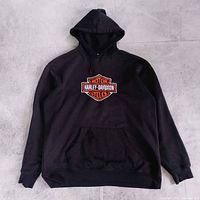 Full front view of black Harley-Davidson hoodie laid flat showing logo, pocket and overall condition.