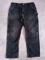 Full view of black Carhartt double-knee work pants lying flat