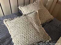 Two cream diamond-pattern fringe pillows on bed
