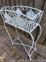 Front angled view of white metal plant stand showing scrollwork and lattice shelf
