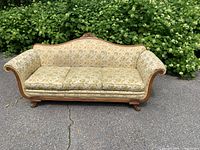 Front view of vintage camelback sofa showing upholstery pattern, carved crest, three seat cushions