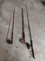 Four fishing rods laid out side-by-side on concrete floor