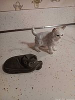 white porcelain cat figurine beside dark stone cat dish