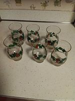 Six clear glasses with holly design and gold rims arranged on countertop