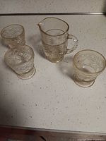 Three dessert cups and one creamer with cut glass patterns on countertop