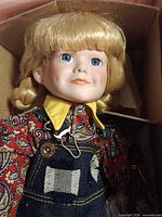 Close-up of doll in box showing facial features, clothing details