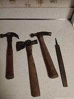 All four tools laid out: two claw hammers, double-bit hatchet, flat file