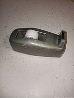 Side view of metal tape dispenser showing roll and cutting blade