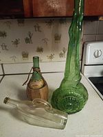 Three bottles on countertop; clear, straw-wrapped, tall green