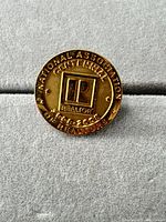 Front view of gold-tone REALTORS centennial pin showing logo and inscriptions