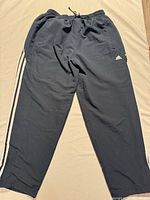 Full view of black Adidas track pants laid flat showing stripes and waistband