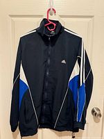 Front view of Adidas track jacket hanging on door