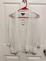 Full view of white open mesh knit cardigan on hanger with tags attached