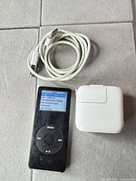 Front view of iPod Nano displaying click wheel, screen on, cable coiled, and AC adapter