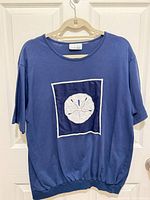Front view of blue pullover top showing embroidered sand dollar applique and overall style