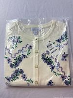 Folded cream cardigan in clear packaging showing floral embroidery, Charter Club label and size tag