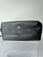 Front view of toiletry bag showing texture, logo badge, faux-leather base