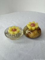 Two tealight holders—clear glass and banded onyx—each containing a yellow flower-shaped tealight candle with pink center, displayed on tabletop