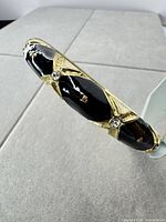 Side view showing black enamel panel, gold X overlay, and rhinestones