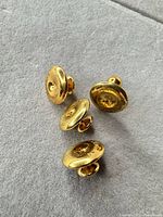 Oblique view of four gold-tone shank cufflinks showing engraved maker’s name and overall design