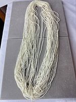 Full view of multi-strand ivory seed bead necklace coiled on display board