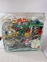 Front view of glass container packed with mixed jewelry pieces