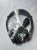 Front view of black over-ear headphones sealed in plastic with coiled cable visible